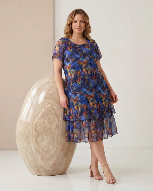 Официална макси рокля от пъстър шифон с разкроен силует, къси ръкави и флорален принт. Представена в цял ръст до голям декоративен камък.