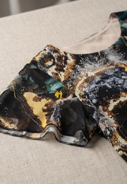 Детайл отблизо на официална рокля от шифон. Ясно се виждат ефирният разкроен ръкав и многоцветният мраморен принт в златисто и тюркоаз.