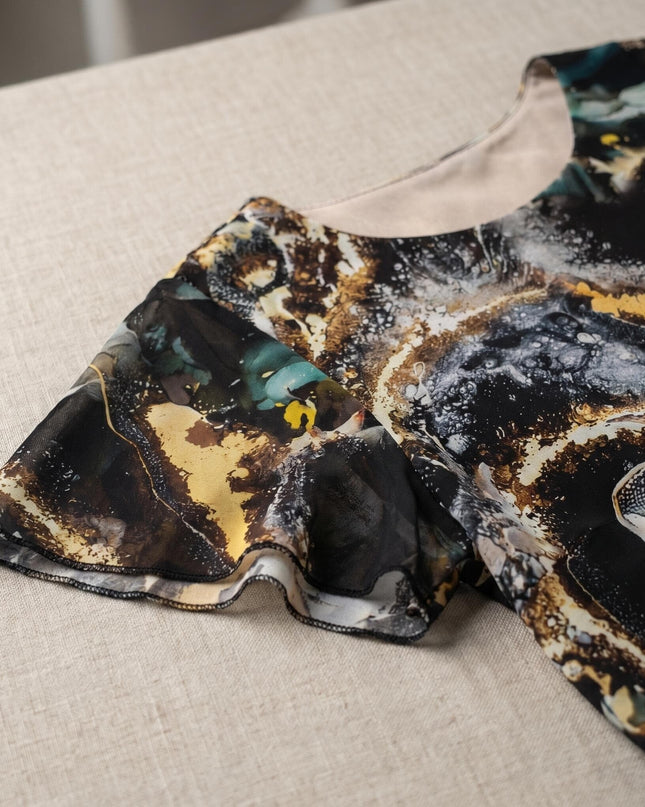 Детайл отблизо на официална рокля от шифон. Ясно се виждат ефирният разкроен ръкав и многоцветният мраморен принт в златисто и тюркоаз.