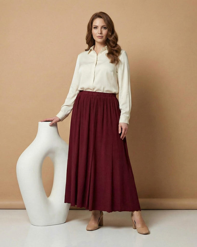 Елегантна дамска разкроена пола в наситено бордо, представена в цял ръст. Моделът е съчетан с бяла риза и позира до декоративна ваза на бежов фон.
