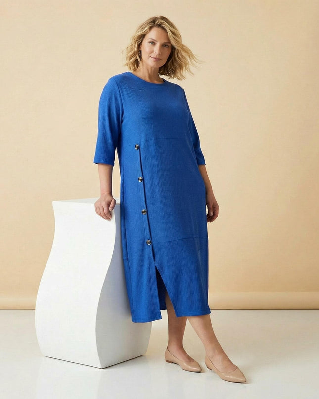 Официална разкроена рокля големи размери в кобалтово синьо, с декоративни копчета и цепка, показана в цял ръст.