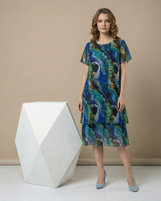 Официална шифонена рокля големи размери в синьо-зелени преливащи тонове. Визия в цял ръст, подчертаваща многопластовия дизайн и облото деколте.