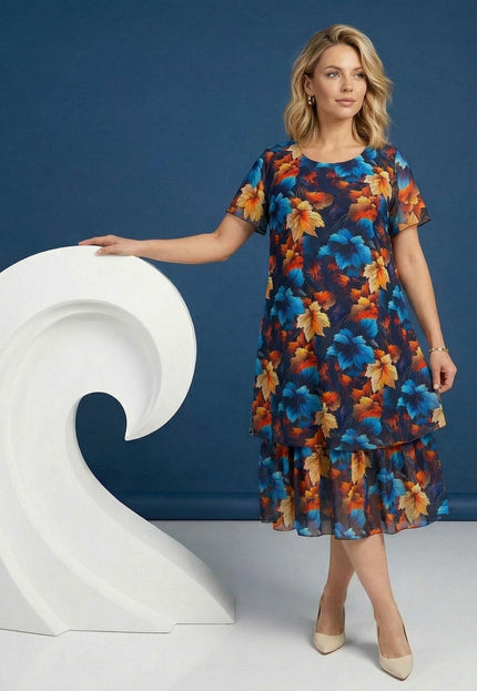 Кадър в цял ръст на жена, облечена в официална тъмносиня рокля от шифон с ефирен многоцветен принт на листа и двуслоен дизайн, на син фон.