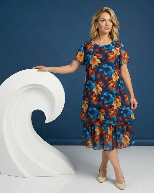 Кадър в цял ръст на жена, облечена в официална тъмносиня рокля от шифон с ефирен многоцветен принт на листа и двуслоен дизайн, на син фон.