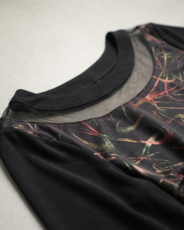 Близък план на деколтето на официална черна туника, показващ прозрачен панел от тюл и цветни абстрактни мотиви върху материята.