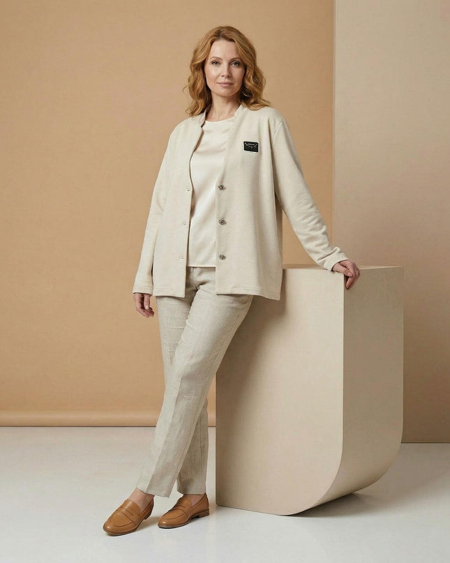 Официално бежово дамско сако големи размери с декоративни копчета и фина емблема. Кадър в цял ръст, представящ елегантна визия с панталон.
