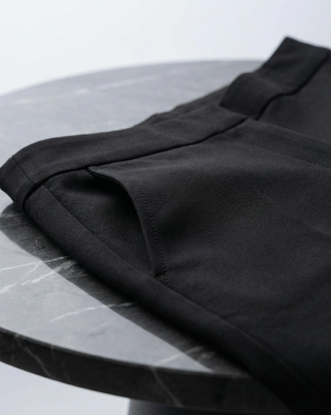 Детайлен кадър на джоба и материята на официален черен панталон в големи размери, сгънат върху мраморна маса.
