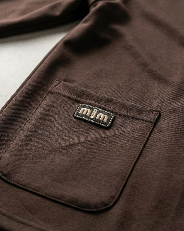 Детайл отблизо на официален дамски комплект в кафяв цвят, показващ преден джоб с декоративен етикет и качествената изработка на шевовете.