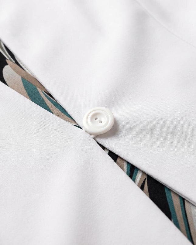 Детайл отблизо на бяло сако с едно копче от официален дамски костюм, показващ част от шарената шифонена рокля.