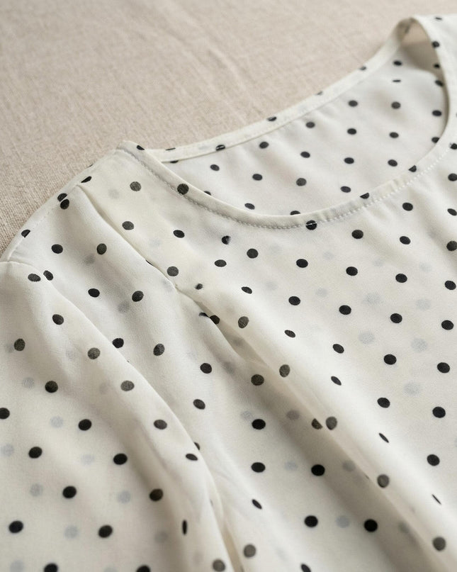 Близък план на деколтето на бяла макси туника на черни точки, разкриващ фината структура на шифона и елегантните набори при раменете.