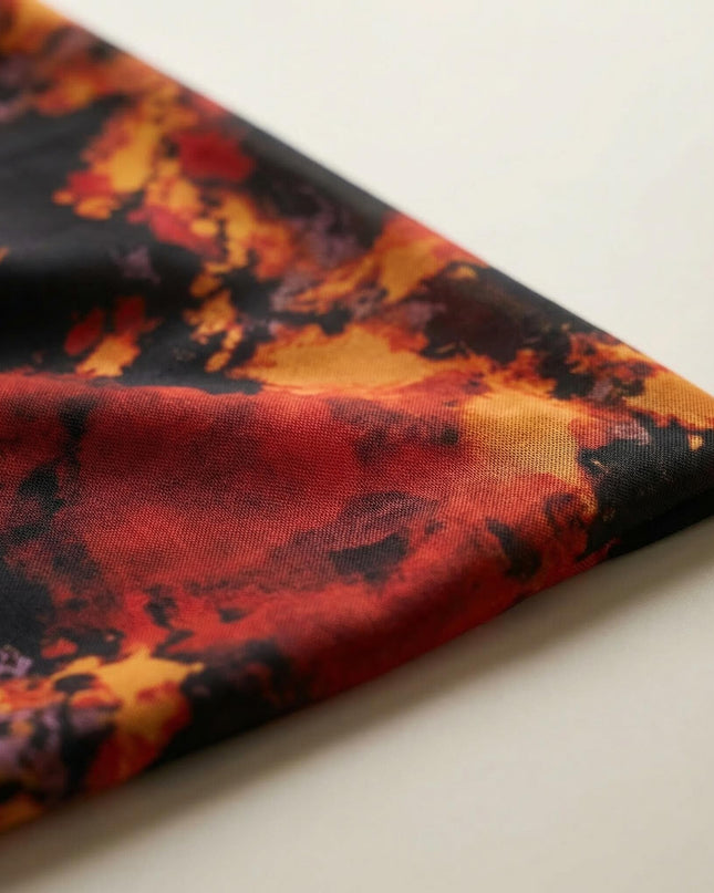 Детайл отблизо на материята на официална макси рокля, показващ ефирния шифон с абстрактен огнен принт на черен фон.