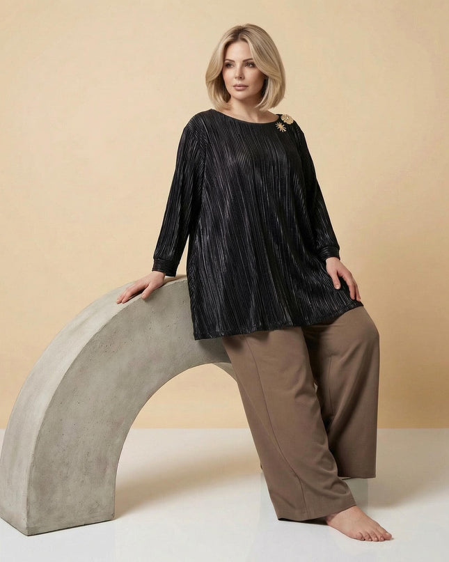 Кадър в цял ръст на модел, носещ официална черна макси туника от плисиран солей с елегантна златна брошка на рамото.