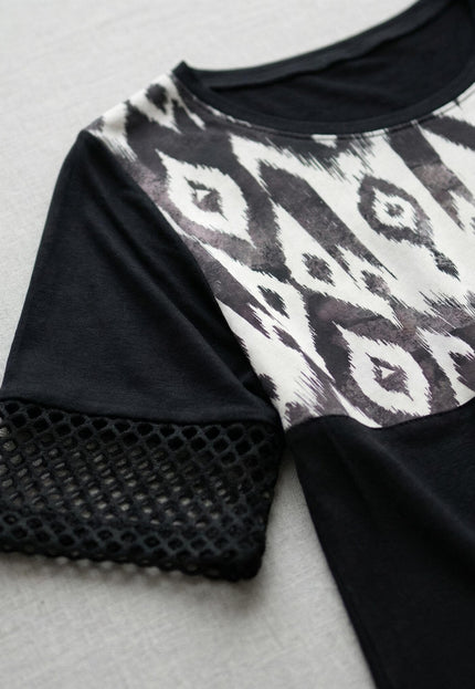 Детайл отблизо на официална черна макси туника, фокусиращ върху облото деколте, ръкава с фина мрежа и контрастния абстрактен принт.