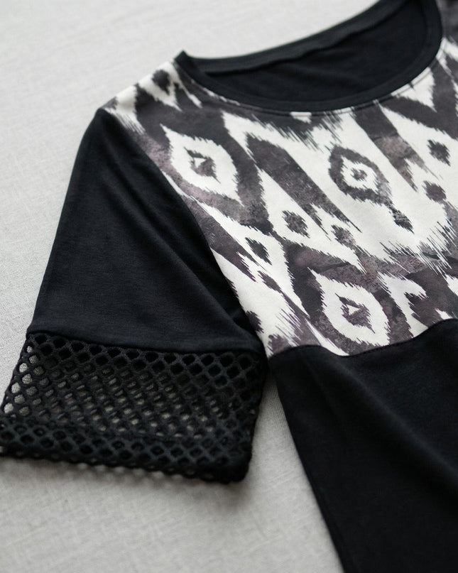 Детайл отблизо на официална черна макси туника, фокусиращ върху облото деколте, ръкава с фина мрежа и контрастния абстрактен принт.