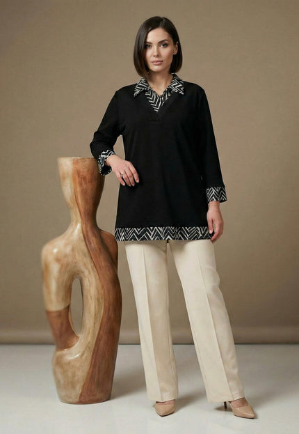 Официална черна туника с яка и маншети на геометрични фигури, заснета в цял ръст до декоративна скулптура.