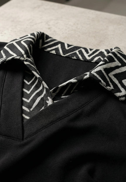 Детайл отблизо на официална черна туника, показващ стилната яка с черно-бял геометричен десен и V-образно деколте.
