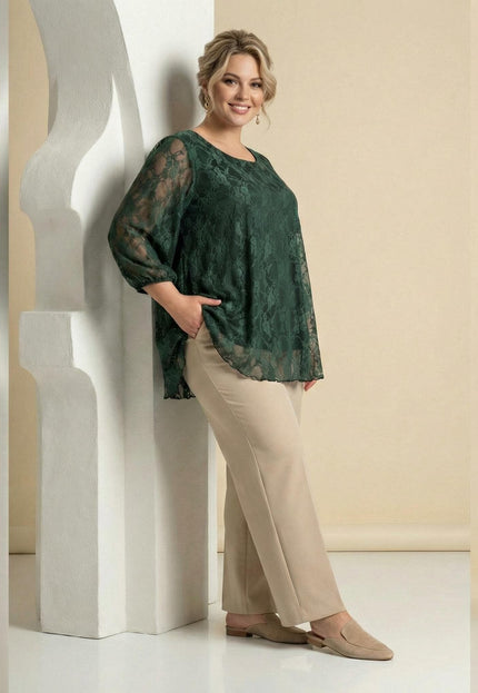 Официална дантелена туника в масленозелен цвят, представена върху модел в цял ръст, облегнат на бяла декоративна колона.