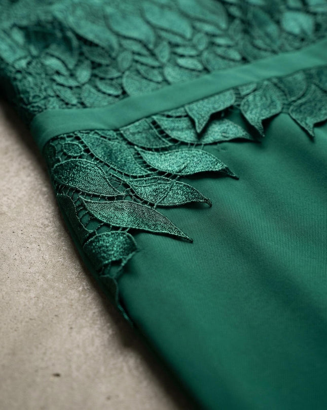 Детайлен кадър на официална макси рокля в масленозелен цвят, показващ отблизо изящната дантела с мотиви на листа и текстурата на плата.