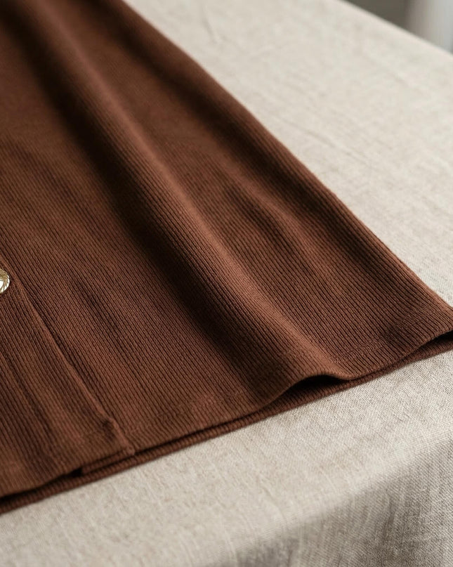 Детайл отблизо на официална макси рокля в кафяво, показващ рипсената текстура на материята и едно декоративно златисто копче.