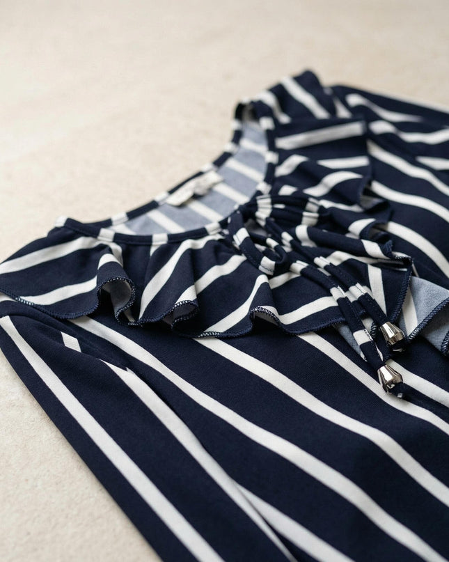 Детайлен поглед към деколтето с връзки и къдрички на официална макси туника на райе, заснета като плосък кадър върху текстуриран фон.