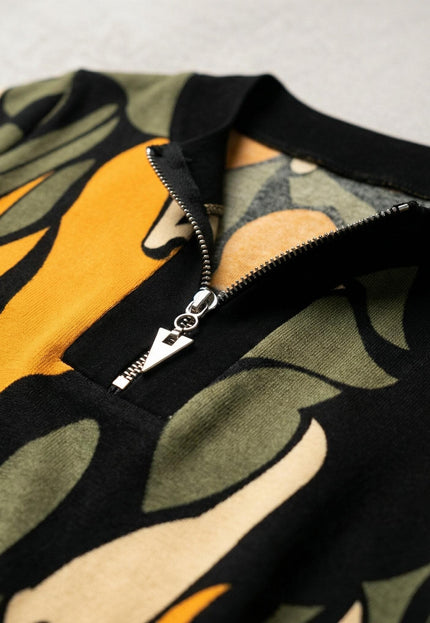 Детайл отблизо на сребрист цип и деколте на официална разкроена макси туника с шарен десен в черно, зелено и жълто.