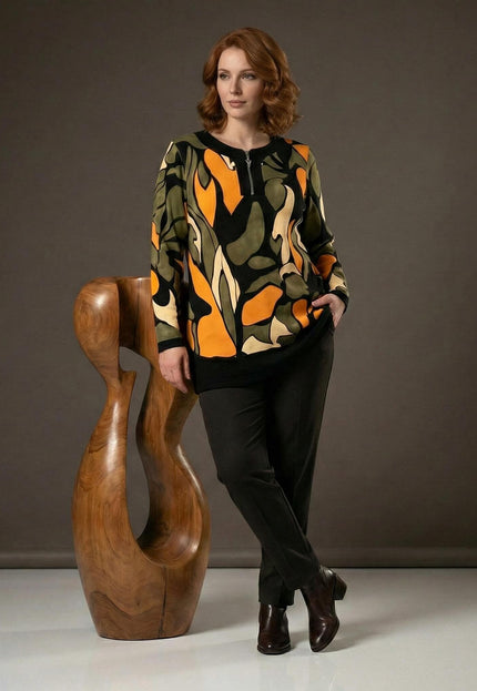 Официална разкроена макси туника с цип в шарен десен, представена върху модел в цял ръст до декоративна дървена фигура.