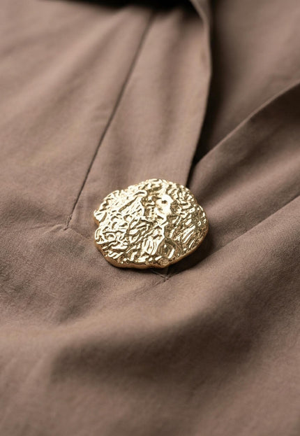 Детайл отблизо на изящния златист елемент при деколтето на официална памучна макси риза в цвят мока.