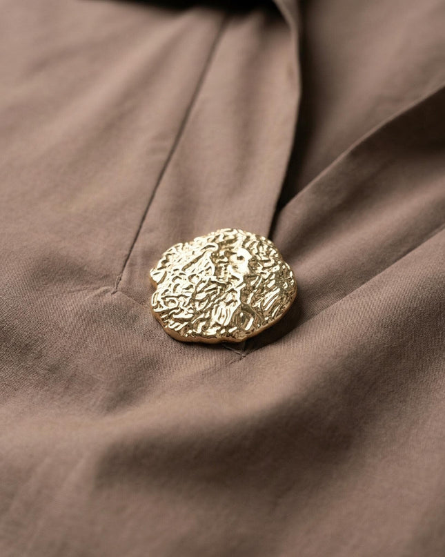 Детайл отблизо на изящния златист елемент при деколтето на официална памучна макси риза в цвят мока.