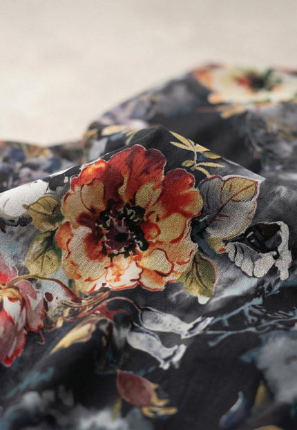 Детайлен кадър отблизо на материята на официална разкроена рокля от шифон, показващ текстурата и живописния флорален принт в червено и жълто.