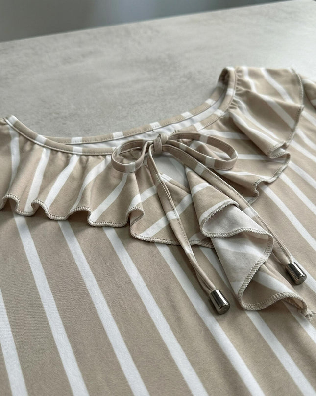 Детайл отблизо на деколте с връзки и волани на официална туника на райе в бежово и бяло, разположена върху плоска повърхност.