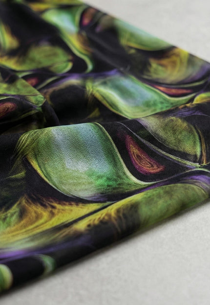 Детайл отблизо на материята на официална шифонена рокля, разкриващ абстрактен десен в наситени нюанси на зелено, лилаво и черно.