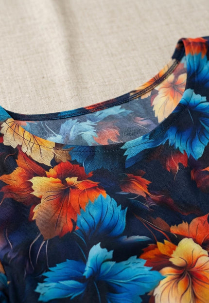 Детайл отблизо на официална тъмносиня рокля, показващ обло деколте и ефирен шифон с многоцветен принт на листа в синьо, оранжево и жълто.