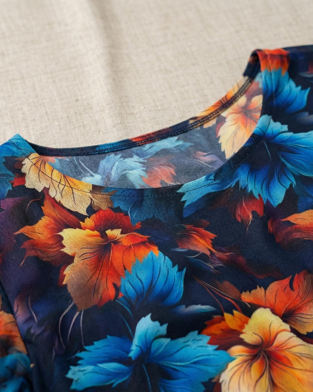 Детайл отблизо на официална тъмносиня рокля, показващ обло деколте и ефирен шифон с многоцветен принт на листа в синьо, оранжево и жълто.