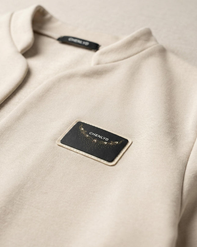 Детайл отблизо на официално бежово дамско сако с ефектно деколте, показващ черна правоъгълна емблема с надпис CHENLYD и декоративни камъчета.