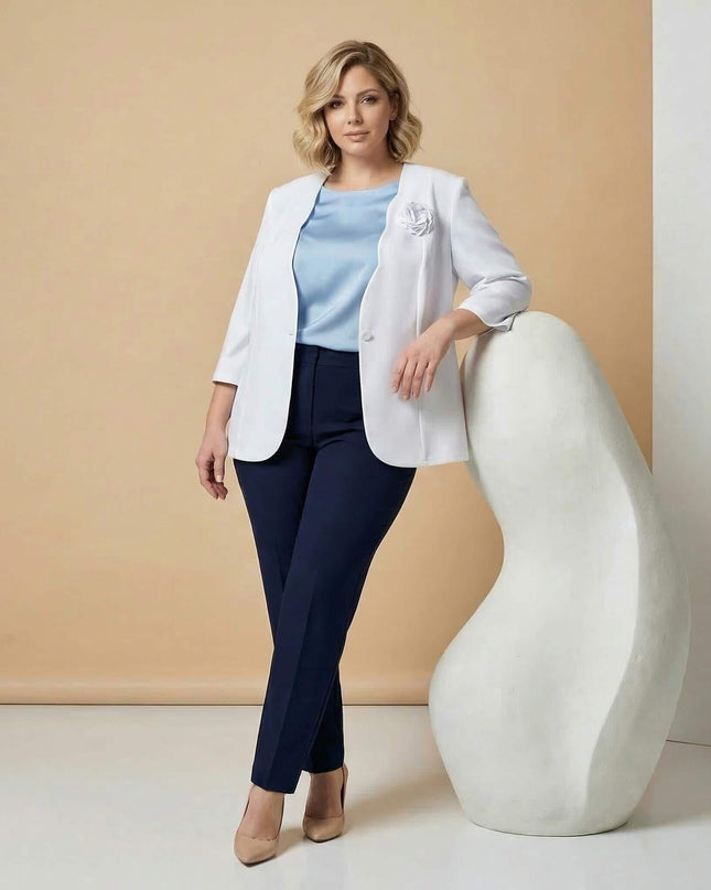 Дамско бяло сако големи размери с нежна брошка роза, представено в цял ръст. Моделът го комбинира елегантно със синя блуза и панталон.