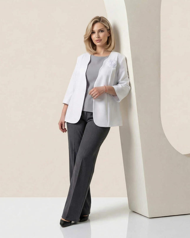 Елегантно дамско бяло сако големи размери с брошка роза и 7/8 ръкав, представено в цял ръст, съчетано със сив топ и тъмносив панталон.