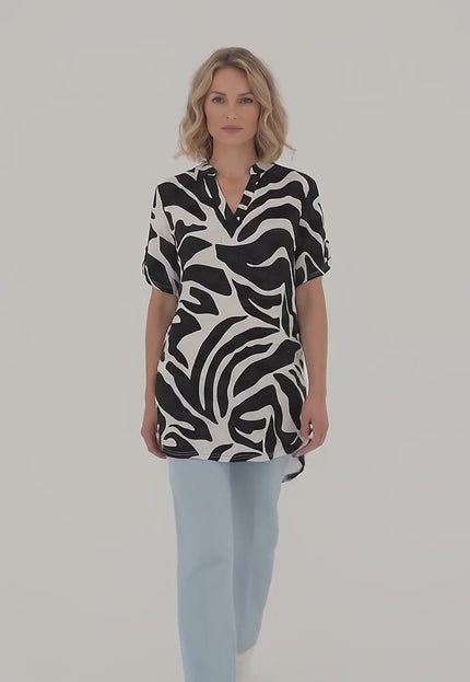 Плюс размер модел носи Макси лятна туника в черно и бяло с асиметрична кройка и върви бавно към камерата на неутрален фон в студийна среда