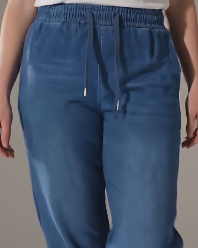 Студийно видео с неутрален фон, в което плюс сайз модел върви бавно към камерата, носейки Сини дамски макси дънки от тенсел с ластик в талията