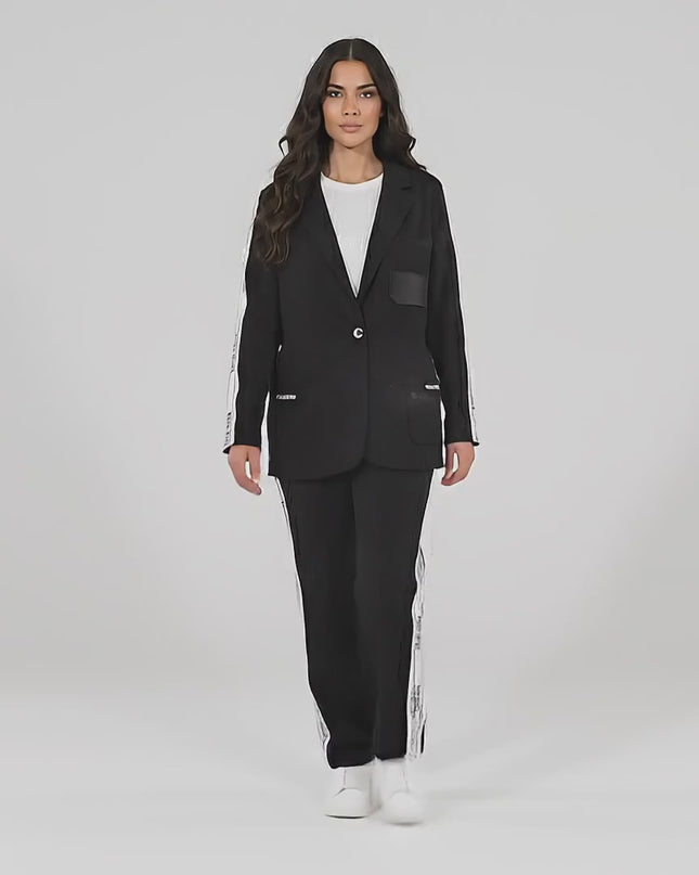 Видео в студийна среда с неутрален фон, на което плюс сайз модел върви бавно към камерата, облечена в Черен ежедневен дамски комплект от две части сако и панталон големи размери