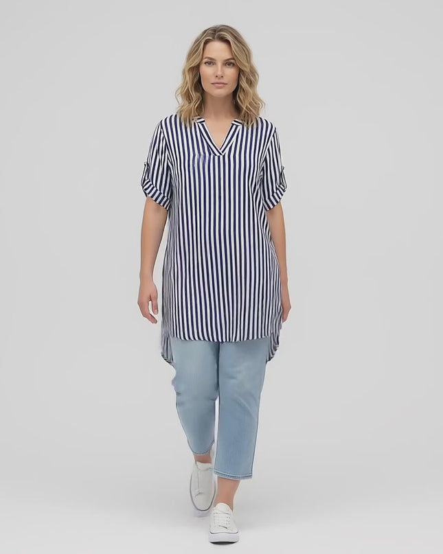 Видео в студийна среда, показващо плюс размер модел, който върви бавно към камерата, облечен с Лятна дамска макси туника в бяло с тъмносиньо райе