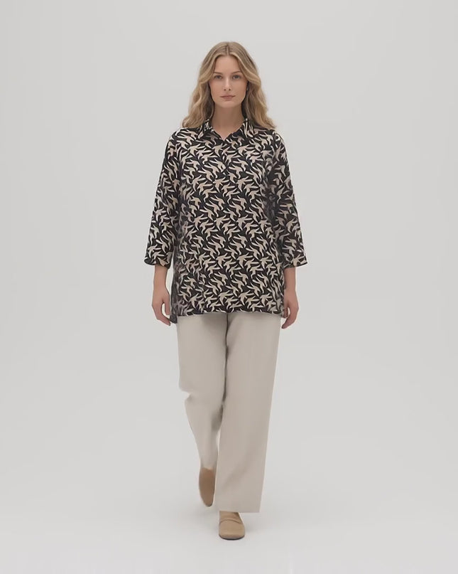 Видео представяне в студио, където плюс сайз модел върви бавно към камерата на неутрален фон, носейки Разкроена официална макси риза с десен в черно и бежово