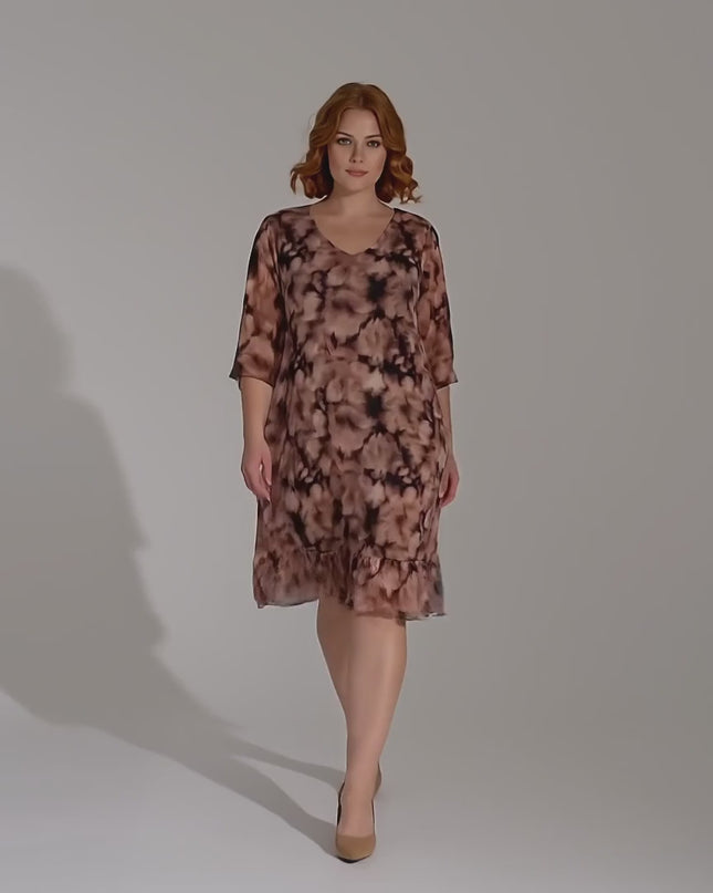 Студийно видео на неутрален фон, в което плюс размер модел върви бавно към камерата, облечена в Официална макси рокля от ефирен шифон с преливащ десен