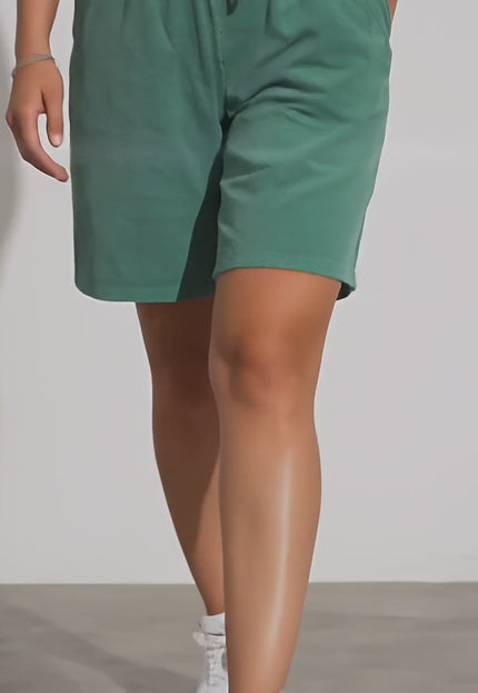 Продуктово видео в студийна среда, показващо плюс сайз модел, който върви бавно към камерата, облечен в Къси шорти с връзки и джобове в зелен цвят и свободна кройка