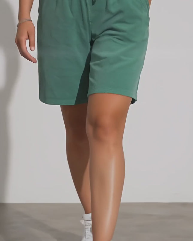 Продуктово видео в студийна среда, показващо плюс сайз модел, който върви бавно към камерата, облечен в Къси шорти с връзки и джобове в зелен цвят и свободна кройка