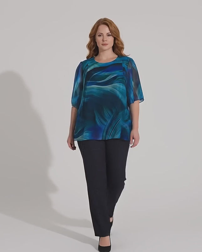 Видео в студийна среда, на което плюс сайз модел върви бавно към камерата, облечена в Официална разкроена макси туника от шифон в синьо с абстрактен принт