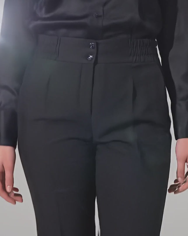 Видео в студийна среда на неутрален фон, в което модел върви бавно към камерата и носи Официален дамски черен панталон с прав крачол и ластик на талията големи размери