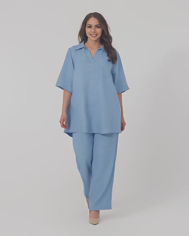 Видео представяне в студийна среда, показващо Kостюм с туника и панталон в големи размери, облечен от модел, който върви бавно към камерата на неутрален фон