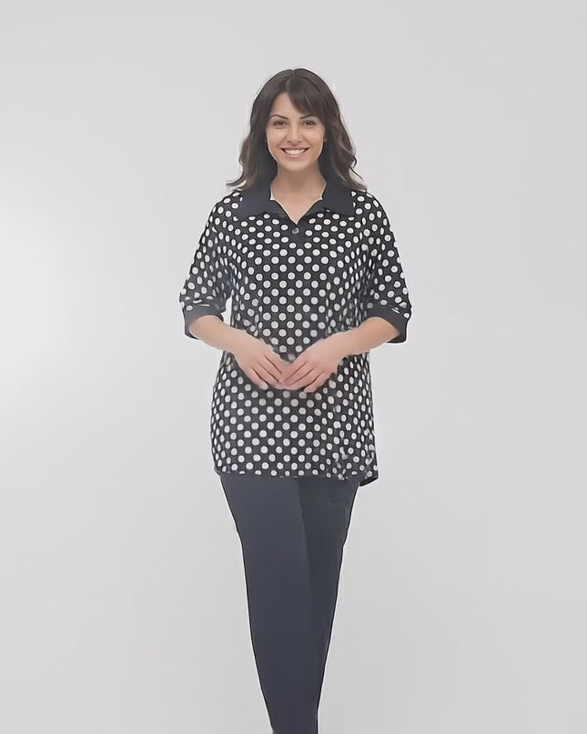 Видео заснето в студио на неутрален фон, показващо макси модел, който върви бавно към камерата, облечен в Официална черна макси туника на бели точки с якичка