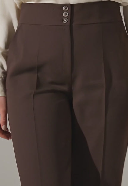 Плюс размер модел крачи бавно към камерата в студийна среда на неутрален фон, носейки Елегантен кафяв панталон с висока талия и копчета големи размери