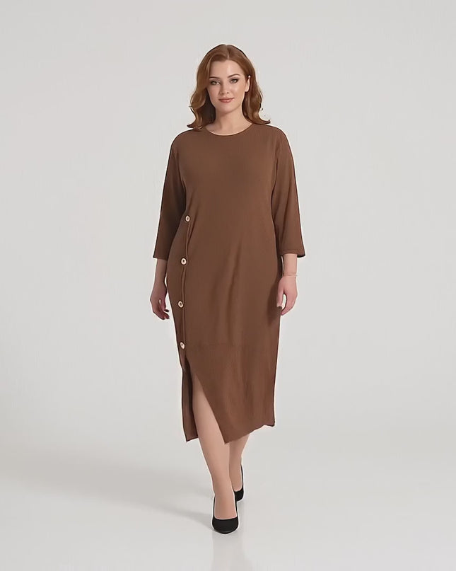 Макси модел върви бавно към камерата в студийна среда на неутрален фон, облечена в Официална макси рокля в кафяво с декоративни копчета